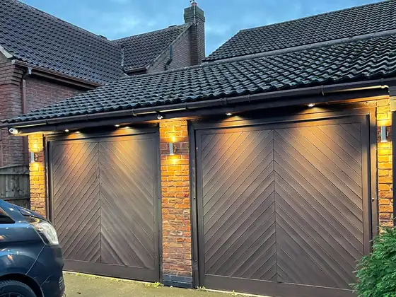 Double garage at dusk lit by downlights and wall lights